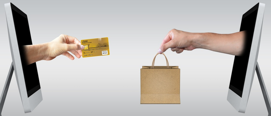 Zwei Hände die aus zwei Monitoren ragen und sich eine Kreditkarte & eine Einkaufstasche für den Cyber Monday Gutscheincode zureichen