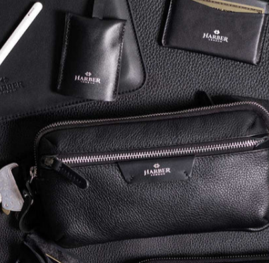 Different Harber London accessories including a card holder, luggage tag, leather desk mat and crossbody bag in black