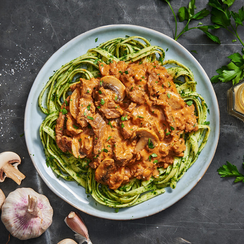 beef stroganoff on a white plate surrounded by mushrooms, herbs and a sprinkle of salt