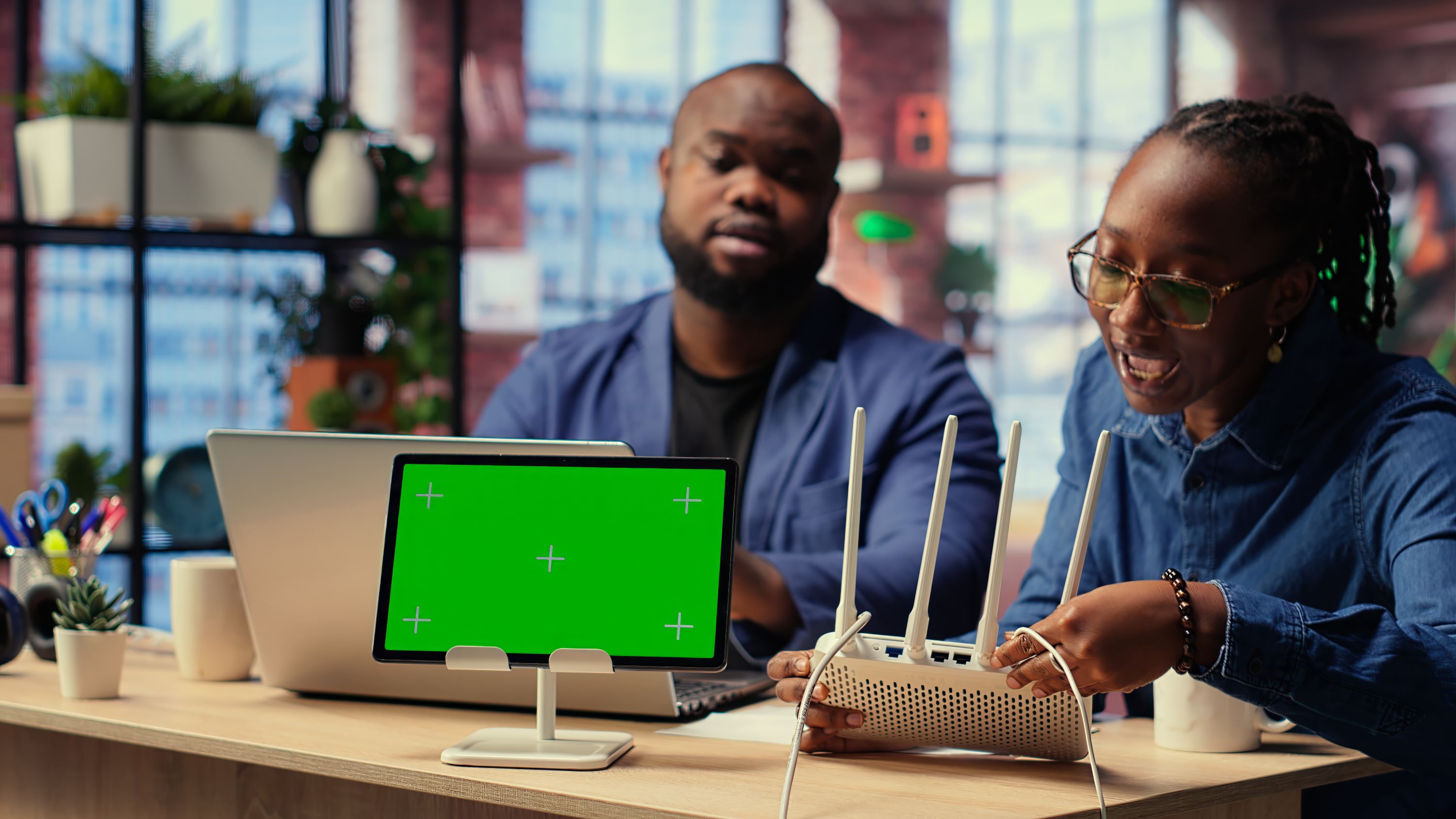 a couple looking at a wifi router with a laptop and tablet on a table