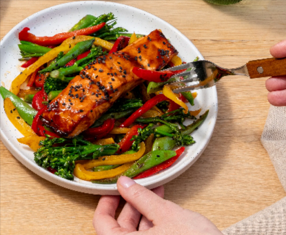 A person eating a pan-seared salmon with vegetables from a Green Chef meal plan