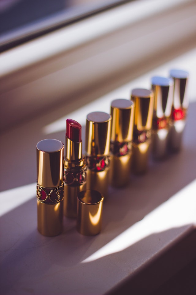 A row of lipsticks in gold and red casing with one cap removed to reveal red lipstick on a table.