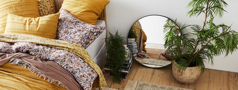 bed, two plants, a stack of books and a mirror resting on a wood floor