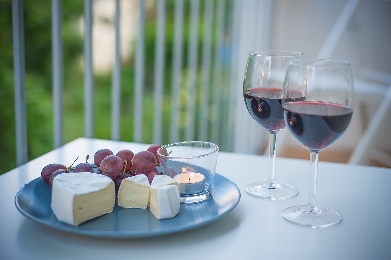 dos vasos de vino rojo con quesos y uvas sobre una mesa en el patio con una atmosfera elegante