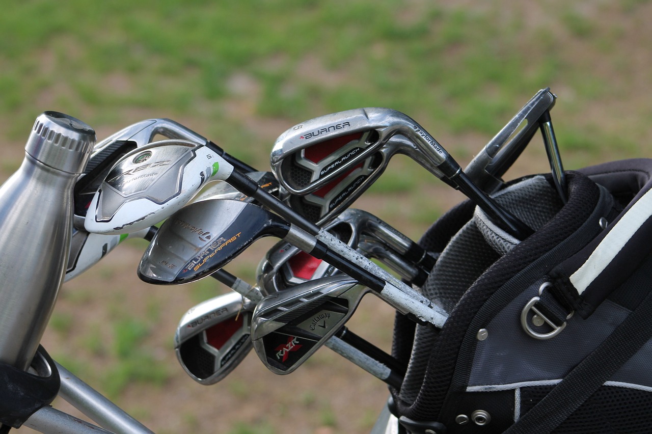 Golf clubs in a golf bag on a green lawn and a silver water bottle.