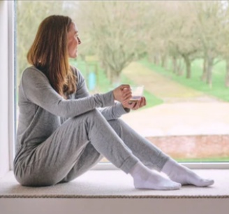 A lady sitting by the window while wearing HJ Hall women's cushioned cotton loose knit diabetic low rise socks
