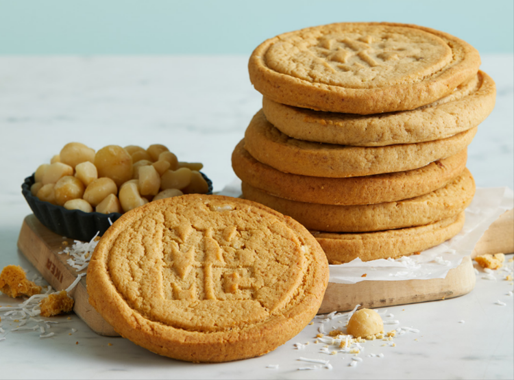 seven cookies and a bowl of macadamia nuts resting on a cutting board on a marble counter