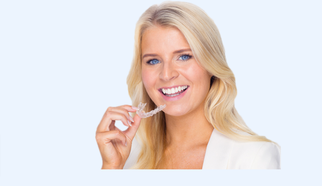 A blonde lady wearing white holding the Straight my teeth aligner and showing her progress