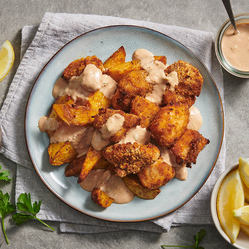 crumbed chicken breasts and roast potatoes on a porcelain plate surrounded by lemon and herbs
