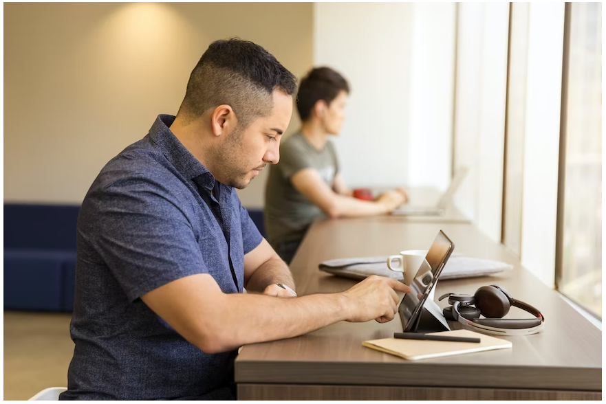 A male student browsing on his iPad for a Croma coupon with his headphones and laptop on the table