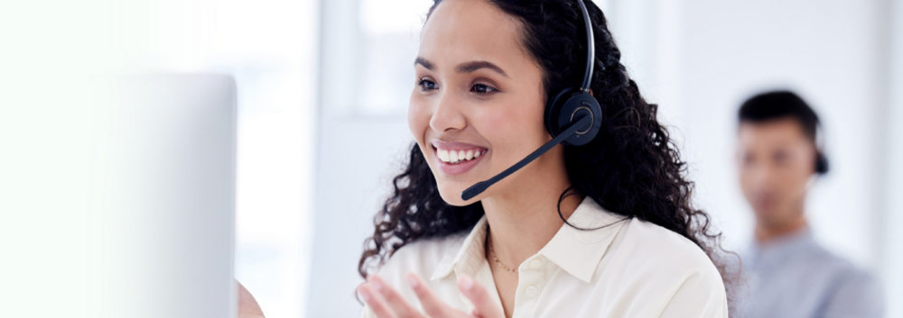 a lady customer service smiling while talking through an earpiece looking at a screen