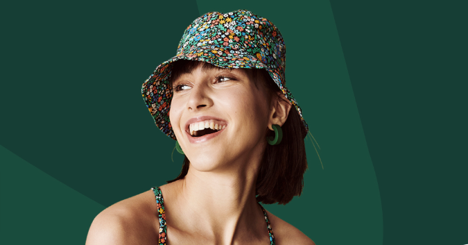 Sparks loyalty program - woman wearing a bucket hat with colourful flowers and smiling over a dark green background.