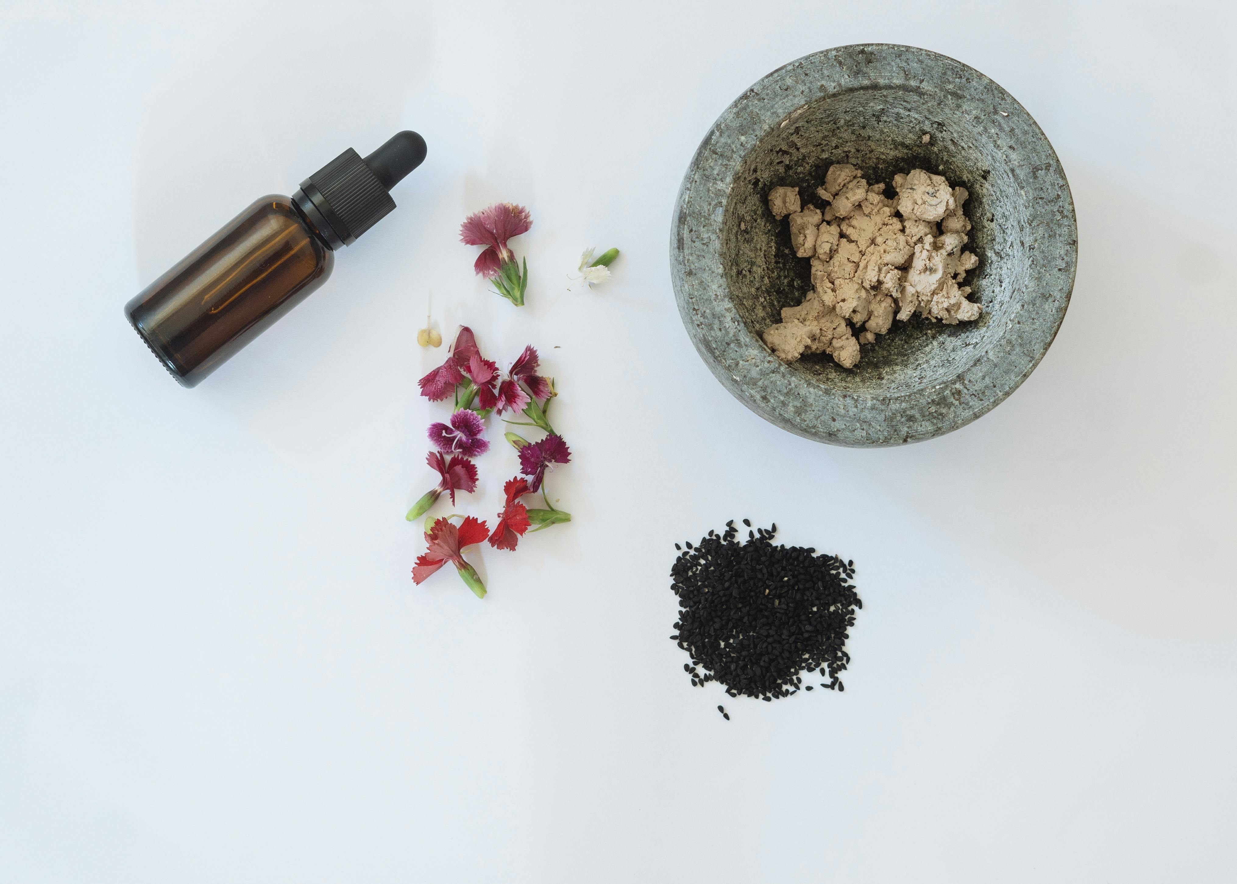 Essential oil in a bottle, flowers, and crushed roots laid out on a flat surface.
