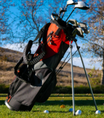 A well-organized golf bag with clubs bought from Gamola Golf on a grassy golf course under clear blue skies.