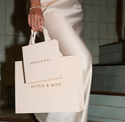 A lady wearing silk and a Astrid & Miyu bracelet while holding {brand shopping bags