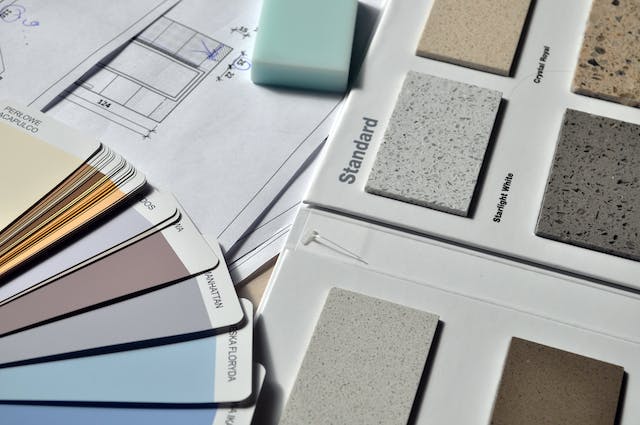 A stack of floor colour samples, some in the form of paint swatches, others in the form of a floor sample board next to floor plans