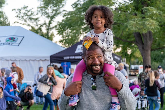 Fun school holiday activities: A girl sitting on her father’s shoulders at the park