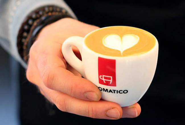 Eine Hand, die eine Kaffeetasse von Aromatico mit einem Herzmuster hält