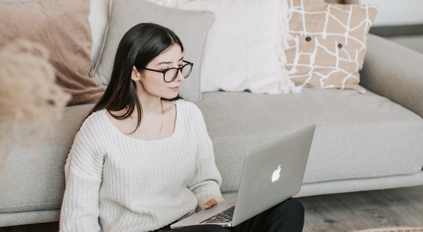 Eine junge Frau mit brille, die vor einer Couch mit einem Laptop hantiert