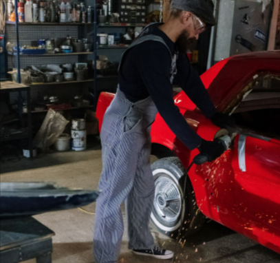 An auto mechanic using a grinder from Frost on a red car, creating sparks in a garage setting