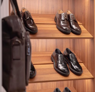 Collection of polished men's dress shoes on wooden shelves in an organised closet.