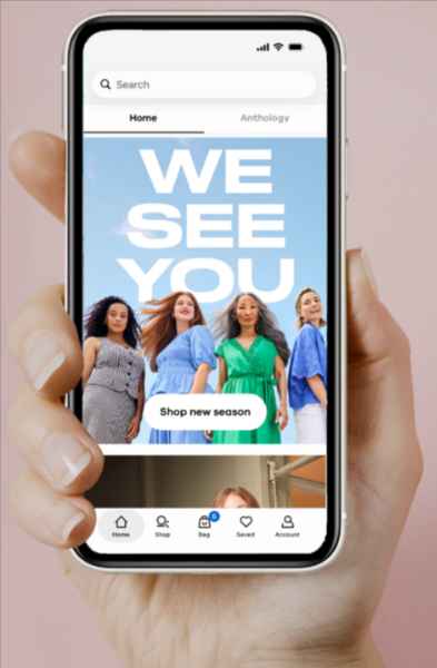 A hand holding a phone showing a fashion app homepage
