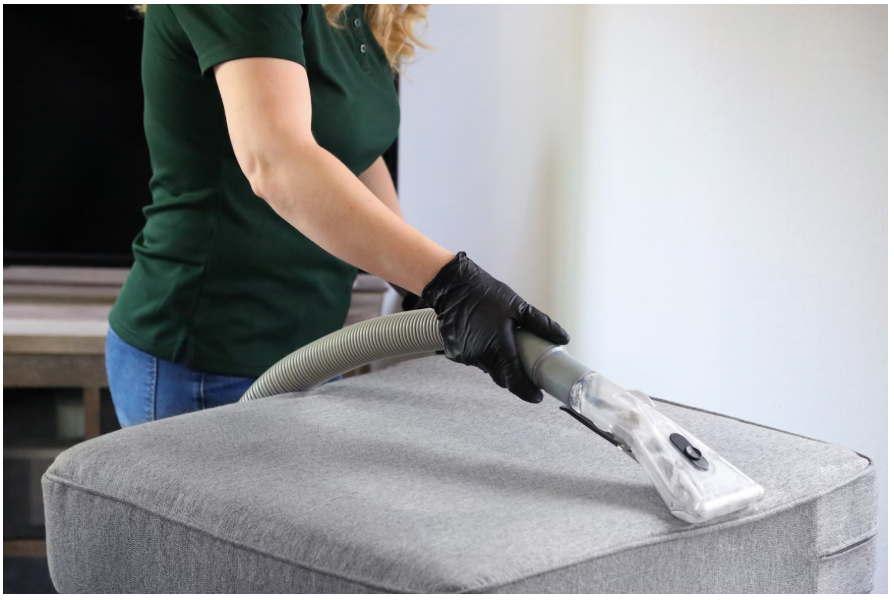 A woman in a gree tshirt and black gloves using a vacuum cleaner