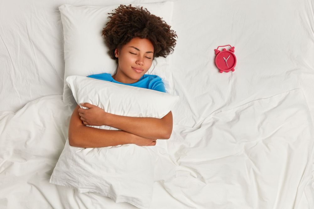 young-brunette-woman-lying-in bed hugging a pillow