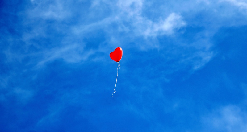 Ein einzelner Herz-Balloon in der Luft unter einem blauen leicht bewölkten Himmel