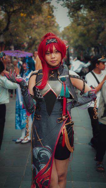 A woman wearing a black and grey costume with red accessories and tassels posing on the street