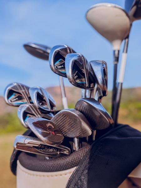A set of golf clubs in a golf bag on a golf course with a blackground of blue sky