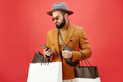 A man smartly dressed and carrying three shopping bags while looking into a phone