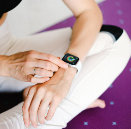A woman adjusting smartwatch from Grade Mobile while sitting on a yoga mat.