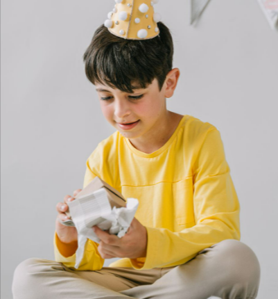 A boy in a party hat joyfully opening a personalised gift ordered from GiftsOnline4u during a birthday celebration.