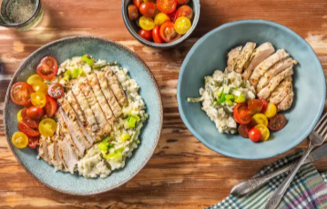 Two plates of grilled chicken with creamy rice and tomatoes