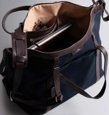 A Harber London navy blue overnight bag with a laptop and sunglasses inside