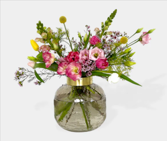 Mixed flower bouquet in a round glass vase with a gold band on a white surface
