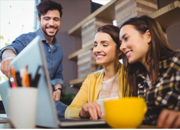Three people sitting and smiling while looking into an open laptop
