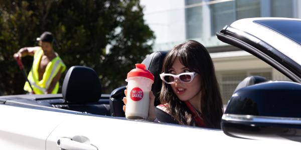 constructuion man in the background and a lady in a car with sunglasses and a The Lady Shake shake in hand