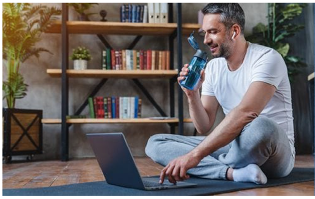 Ein sitzender Mann mit einer Wasserflasche, der einen Laptop bedient