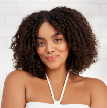 A woman wearing a white top and wearing out her curly hair after using the Bumble and bumble curl range