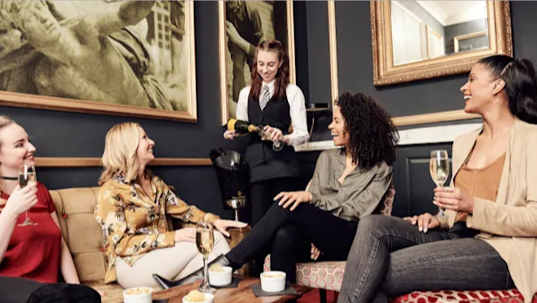 Four ladies sitting and smiling while a waitress pours champagne into their glasses