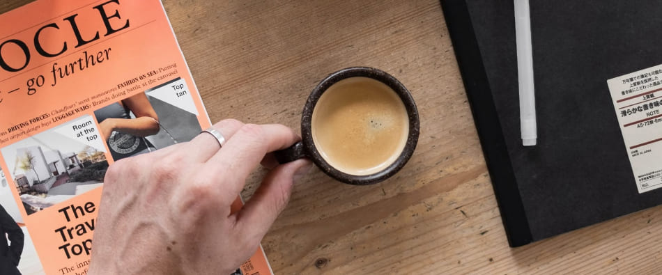 A man placing a mug of coffee down on a wooden table between a pair of books