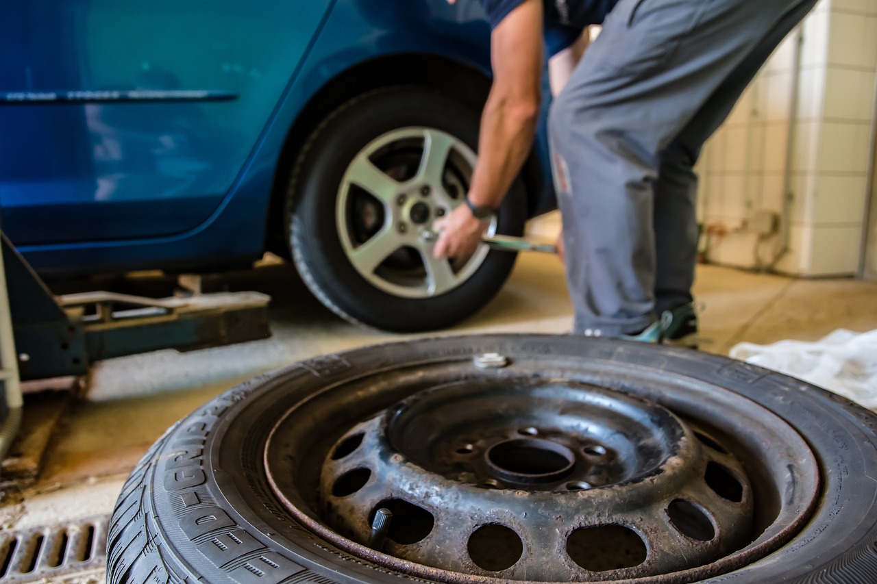 mecánico arreglando una rueda de un coche azúl en un taller con fondo claro de día