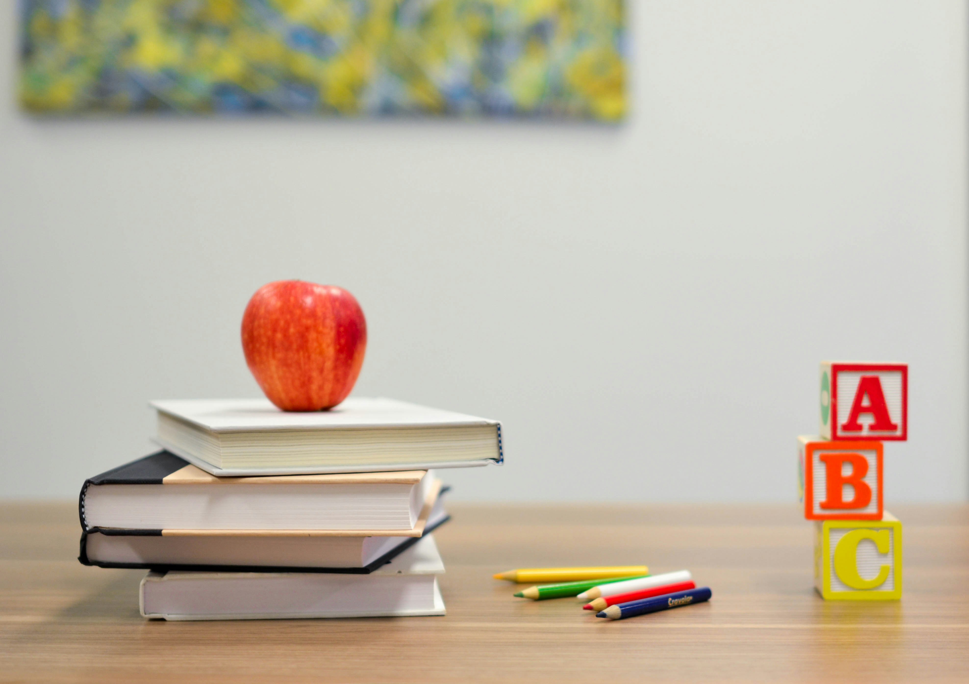 red apple on top of stacked books with pens on the table