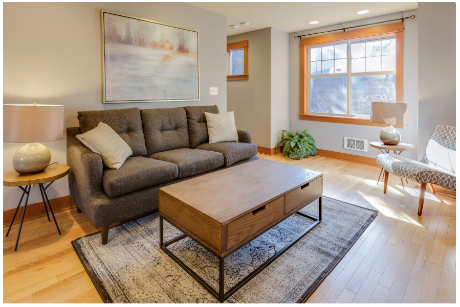 A couch with two white pillows and a coffee table on a rug