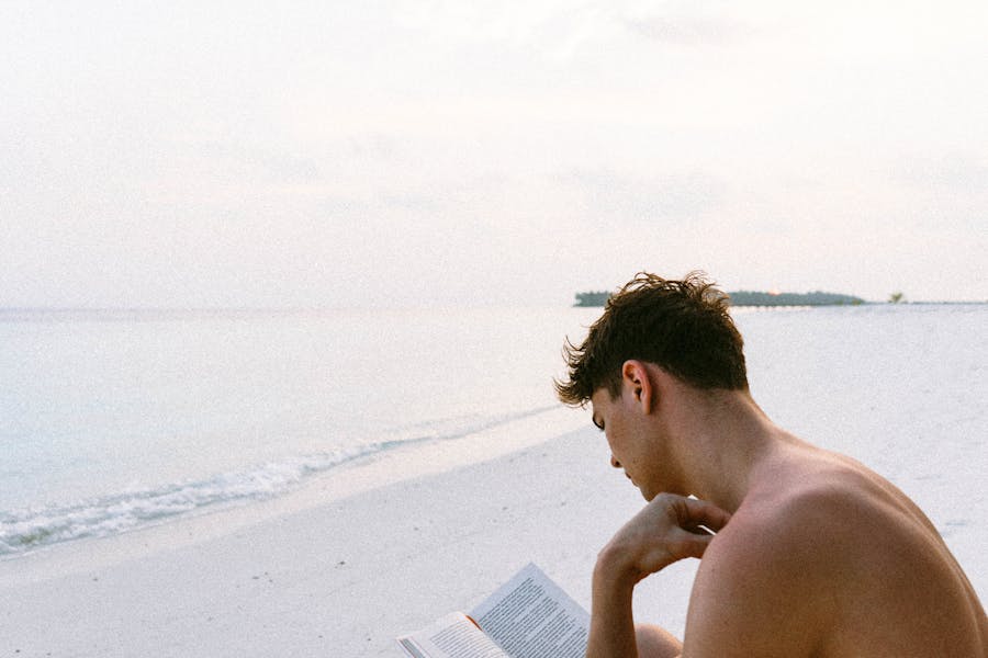 Topless man reading a book on the beach by himself