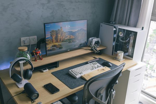 Modern gaming and work desk setup with a monitor, keyboard, PC tower, PlayStation, and headphones