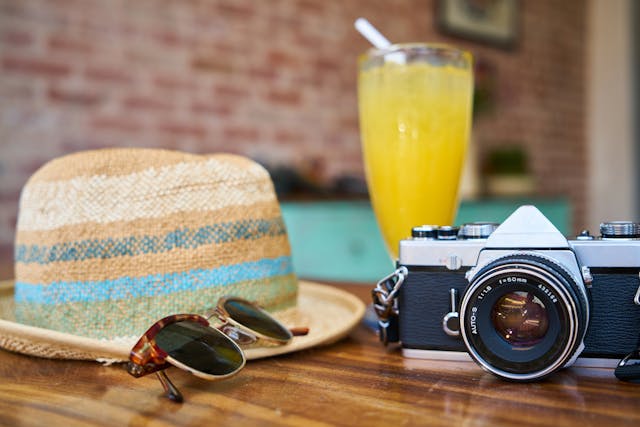 A sun hat, camera, glasses and drink on a wooden table in a restaurant