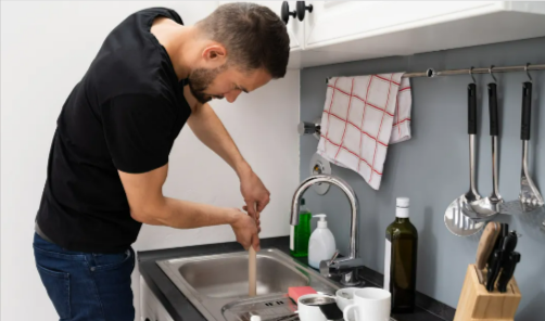 A person trying to unplug a clogged kitchen sink